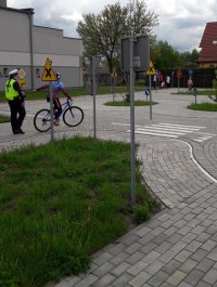 Policjantka ruchu drogowego na miasteczku rowerowym ocenia uczestnika turnieju, który porusza się na rowerze.