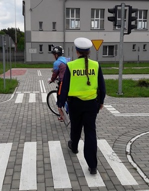 Policjantka ruchu drogowego ocenia ucznia poruszającego się rowerem po miasteczku ruchu drogowego.