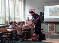 Policjant wręcza dzieciom książeczkę o bezpieczeństwie na drodze.