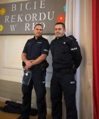 Dwóch policjantów stoi pod tablicą na której widnieje duży napis bicie rekordu w RKO