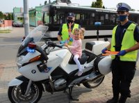 Dziewczynka siedzi na policyjnym motorze, obok stoją policjanci