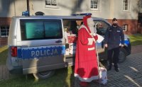 mikołajkowa wizyta policjantów w domu dziecka - na zdjęciu radiowóz, paczki, policjant i mikołaj