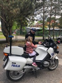 Policjant tłumaczy dziewczynce siedzącej na motocyklu do czego służą konkretne przyciski
