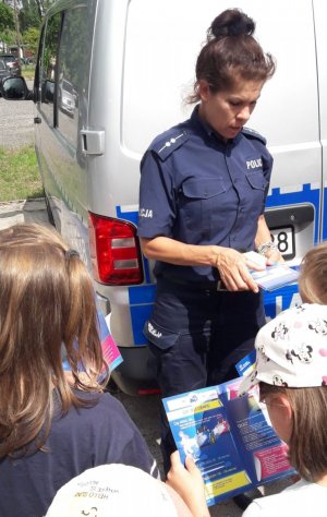 policjantka wręcza dzieciom ulotki dotyczące bezpieczeństwa w ruchu drogowym