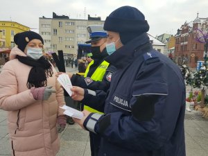 Policjanci podczas świątecznego jarmarku wręczają mieszkańcom opaski odblaskowe i zawieszki do prezentów