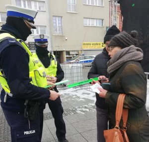 Policjanci podczas świątecznego jarmarku wręczają mieszkańcom opaski odblaskowe i zawieszki do prezentów