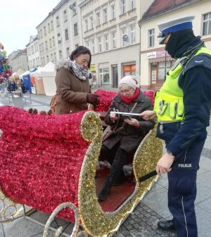 Policjanci podczas świątecznego jarmarku wręczają mieszkańcom opaski odblaskowe i zawieszki do prezentów