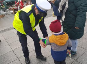 Policjanci podczas świątecznego jarmarku wręczają mieszkańcom opaski odblaskowe i zawieszki do prezentów