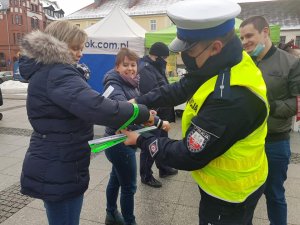 Policjanci podczas świątecznego jarmarku wręczają mieszkańcom opaski odblaskowe i zawieszki do prezentów