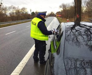 Policjant ruchu drogowego wręcza kierowcy ulotkę