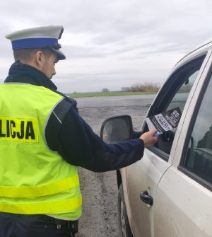 Policjant ruchu drogowego wręcza kierowcy ulotkę