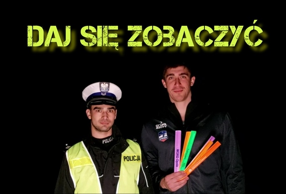 policjant z ruchu drogowego stoi obok zawodnika Grupy Azoty ZAKSA Kędzierzyn-Koźle, który trzyma w ręku odblaski, nad nimi hasło &quot;Daj się zobaczyć&quot;