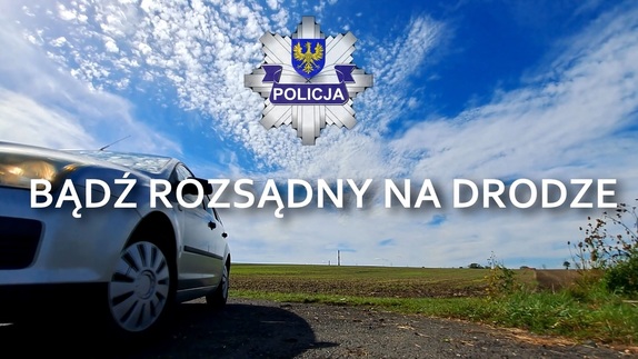 srebrny samochód, w tle trawa i niebo, na środku logo Opolskiej Policji i napis &quot;bądź rozsądny na drodze&quot;