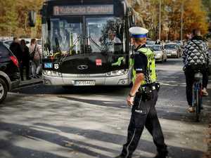 na zdjęciu policjant ruchu drogowego, w tle autobus, rowerzysta, pojazdy i piesi