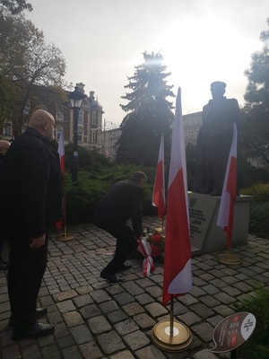 na zdjęciu dwie osoby, jedna z nich składa kwiaty pod pomnikiem