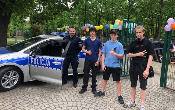 na zdjęciu policjant i trzech nastolatków, za nimi radiowóz