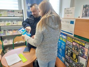 Policjanci na stanowisku informacyjnym w urzędzie pracy informują o trwającym doborze. Na stole leżą ulotki