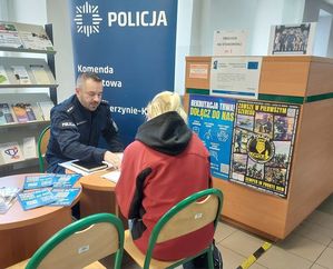 Policjanci na stanowisku informacyjnym w urzędzie pracy informują o trwającym doborze. Na stole leżą ulotki