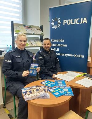 Policjanci na stanowisku informacyjnym w urzędzie pracy informują o trwającym doborze. Na stole leżą ulotki