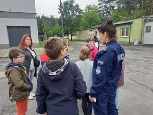 Grafika przedstawia dzieci oprowadzane po komendzie policji