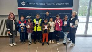 Grafika przedstawia dzieci oprowadzane po komendzie policji