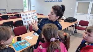 Grafika przedstawia dzieci oprowadzane po komendzie policji