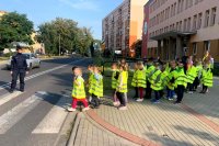 Dzieci ubrane w kamizelki odblaskowe pod opieką policjantki i nauczycielek przechodzą przez przejście dla pieszych