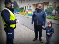 Policjant który ma w ręku odblaski stoi na przeciwko mężczyzny, który trzyma za rękę chłopca