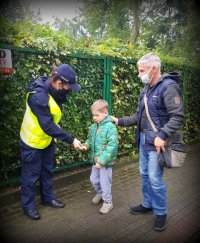 Policjantka na chodniku wręcza odblask chłopcu, obok którego stoi mężczyzna